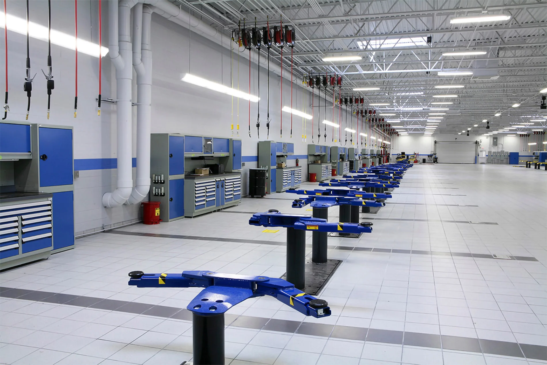 An automotive service center with multiple vehicle lifts, tool cabinets, and overhead pneumatic hoses